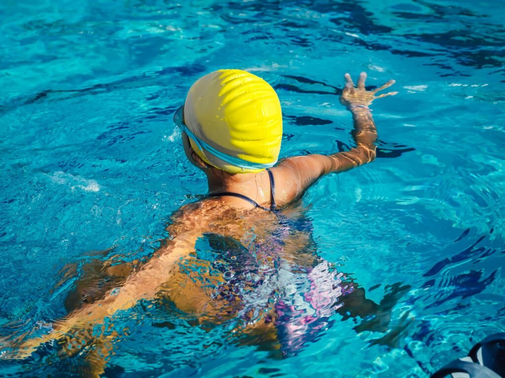 A swimmer wearing a yellow cap enjoying a pool swim captured from the back, highlighting effective technique.
